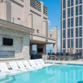 rooftop pool at Atlantic House Midtown, offering a resort-style experience with sleek in-water loungers, a modern stone-accented wall featuring an outdoor TV, and a stylish bar area with high-top seating. Set against the backdrop of Atlanta’s skyline, this luxurious space is designed for both relaxation and socializing in an upscale urban setting.