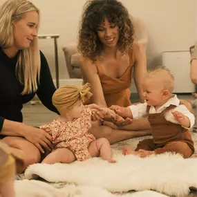 Two moms playing on a rug with their newborns