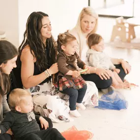 New moms sit on the floor with their infants learning from the class instructor