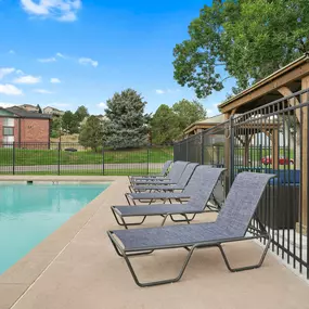 A pool with lounge chairs and a fence.