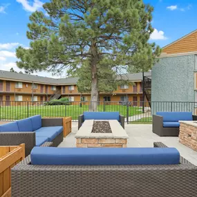 A large tree is in the middle of a patio with blue couches and wooden tables.