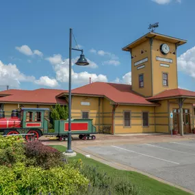 Exterior shot of the Edmond dental clinic with landscaping in the foreground, a model train, and a yellow exterior building with a clock tower.