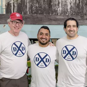 Dr. Glenn, Dr. Milson, and Dr. Patel smile at the camera while wearing Dental Depot shirts