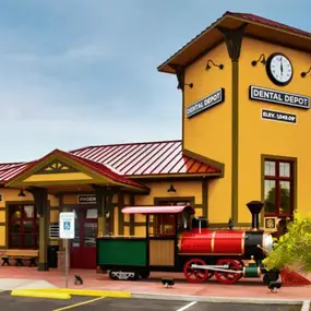 Exterior view of the Dental Depot dentist office in West Phoenix with a clock tower, model train, red roof, and yellow exterior.