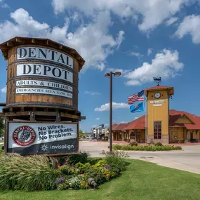 Exterior image of the Dental Depot dental clinic in North OKC with a clock tower in the foreground, yellow exterior, clock tower, and red roof.
