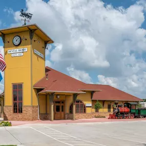 Exterior image of Dental Depot's North OKC dental clinic with a flagpole, clock tower, model train, and yellow exterior.