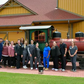 The Tulsa Hills dental team poses in front of the model train outside the Tulsa Hills dental clinic