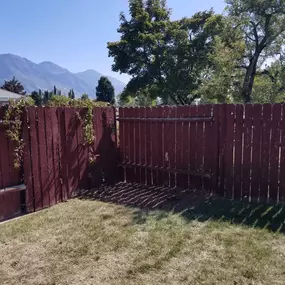 Red wooden fence in backyard with trees, mountains, and grass.