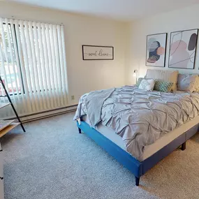 A bedroom with a bed, nightstand, and a window with blinds