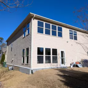 Back Exterior View of Two-Story Home with Large Windows

This rear exterior view of a two-story home showcases beige horizontal siding and a clean, modern layout with abundant windows for natural light. The lower level features a full wall of windows and a glass exterior door, perfect for a future sunroom, home office, or patio access. The upper level includes multiple matching windows, enhancing energy efficiency and providing panoramic backyard views. Set on a gently sloped lot with minimal la