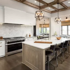 Modern Farmhouse Kitchen with Custom Island and Designer Lighting

This beautifully designed modern farmhouse kitchen features a custom wood island with quartz countertops and stylish black bar stools, perfect for casual dining or entertaining. The white cabinetry, shiplap-style range hood, and herringbone marble backsplash create a clean, timeless look. Rustic wood ceiling beams and geometric pendant lights add warmth and architectural interest. Stainless steel appliances and an open layout sea