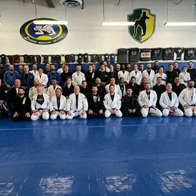 Large group of Brazilian Jiu-Jitsu practitioners posing for a photo inside a training facility with blue mats, wearing gis and rash guards, under the Zingano Brazilian Jiu-Jitsu logo on the wall.
