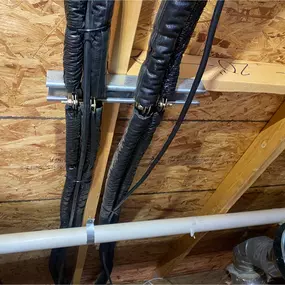 Insulated refrigerant lines neatly secured to attic trusses with metal brackets, demonstrating HVAC line set installation by Perry Mechanical Inc.