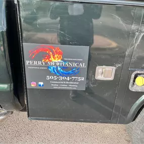 Close-up of a black work truck door displaying the Perry Mechanical Inc. logo, highlighting services in heating, cooling, and plumbing.