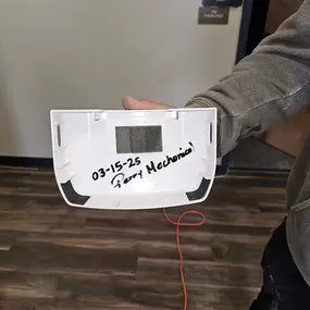 A white HVAC panel held by a technician, marked with '03-15-25 Perry Mechanical' to indicate service date and provider.