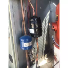 Close-up view inside an HVAC unit showing copper refrigerant lines with a black suction line accumulator and a blue filter drier, part of a cooling system installation or repair by Perry Mechanical Inc.