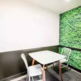 A white table with two chairs in front of a green plant wall.