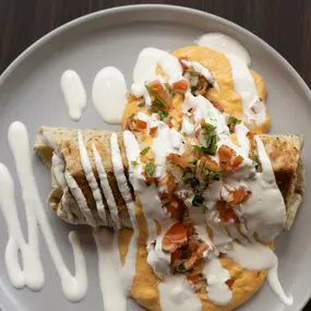 A delicious plate of enchiladas topped with fresh pico de gallo, drizzled generously with creamy white sauce, and garnished with herbs for a vibrant finish.