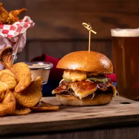 A mouthwatering burger piled high with toppings is paired with crispy onion rings and a refreshing pint of beer, served on a rustic wooden board for the ultimate pub-style meal.