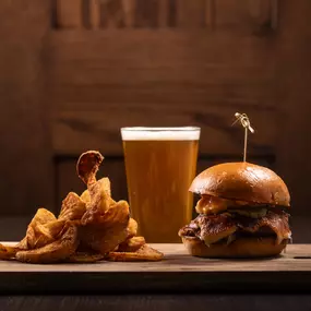 A mouthwatering burger piled high with toppings is paired with crispy onion rings and a refreshing pint of beer, served on a rustic wooden board for the ultimate pub-style meal.