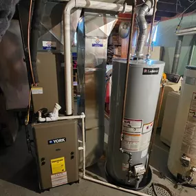 A basement utility area featuring a York furnace and Lochinvar water heater, with connected ductwork, pipes, and ventilation system.