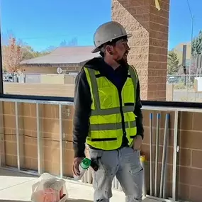 Three crew members from Nichols Mechanical stand inside a partially constructed building, likely a commercial project. They’re wearing hard hats, high-visibility safety vests, and work gear while discussing the job at hand. Metal framing and conduit lines are visible, along with an open window space that shows nearby buildings under a clear blue sky. The scene reflects teamwork and professionalism on a construction site.