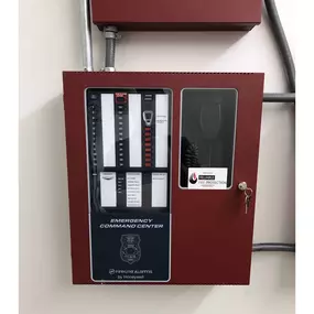 Red emergency command center panel with black and white controls, a key lock, and an attached microphone on the right. The label reads 