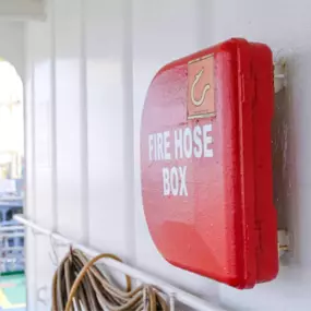 Red fire hose box mounted on a ship wall near coiled hoses.