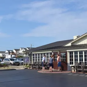 Front view of Miller’s Seafood & Steakhouse in Kill Devil Hills, NC, with guests entering the building, outdoor seating, and a sign advertising breakfast, Alaskan crab legs, and hand-rolled sushi.