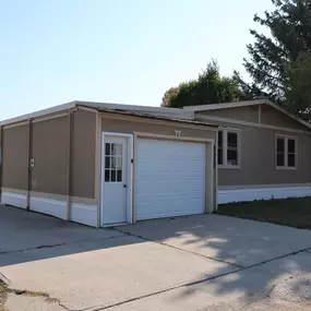 An exterior view of a beige mobile home and a beige garage that has a white door.