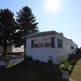 An exterior view of few mobile homes with trees and lawns with potted plants.