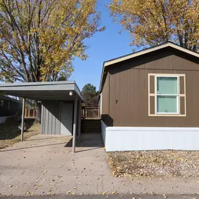 An exterior view of a brown and white mobile home and a carport