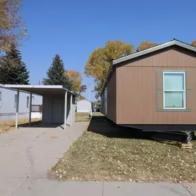 The exterior view of a brown mobile home with a driveway and a carport.