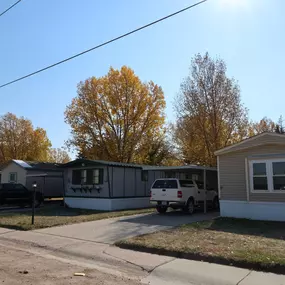 A row of mobile homes on a street and cars in the carports of each mobile home.