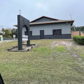 The updated exterior of 3 Brothers Painting & Home Improvements, LLC features a sleek gray and black color scheme on the building and brick arch sign, set against an overcast sky and trimmed landscape.