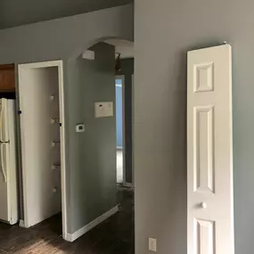 This freshly painted interior hallway by 3 Brothers Painting & Home Improvements, LLC showcases smooth gray walls, white trim, wood-look flooring, and a detached white closet door awaiting reinstallation.