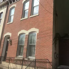 A red brick townhouse with arched windows, beige stone trim, and black wrought iron railings. A black door with a lantern.