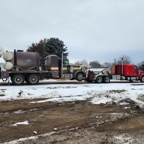 A red tow truck from 4 States Towing hauls a large vacuum tanker truck on a snowy rural road.