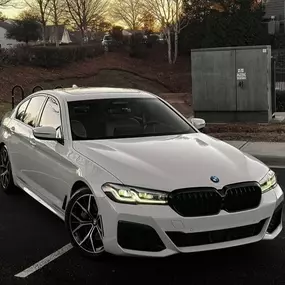 Pristine white BMW 5 Series sedan gleaming after professional auto detailing service, parked outdoors.