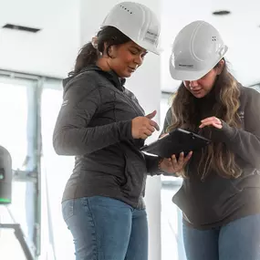 Zwei Projekt Kraft Mitarbeiterinnen mit Schutzhelmen besprechen mithilfe eines Tablets ein Bauprojekt im Innenausbau.