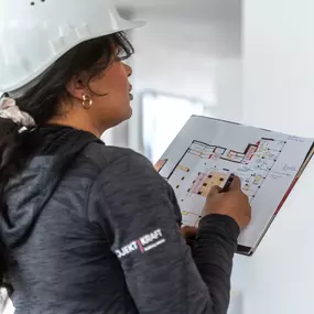 Projekt Kraft Mitarbeiterin mit Schutzhelm analysiert einen Bauplan auf der Baustelle eines Innenausbau-Projekts.