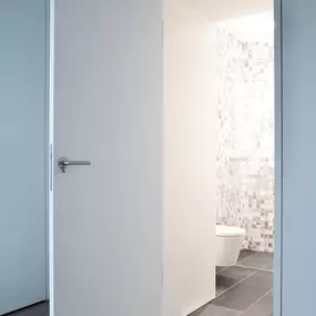 Einblicke in ein durchdachtes Raumkonzept: Die geöffnete, wandbündig integrierte Tür gibt den Blick frei auf ein modernes Bad mit Mosaikfliesen und wandhängendem WC. Die klare Linienführung, die reduzierte Farbgebung und die hochwertigen Materialien unterstreichen den minimalistischen Charakter des Entwurfs.