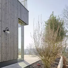 Detailansicht des modernen Anbaus mit vertikaler Holzverschalung, großzügiger Glasfassade und klar gegliederter Außenanlage. Architektur und Landschaftsgestaltung greifen harmonisch ineinander.