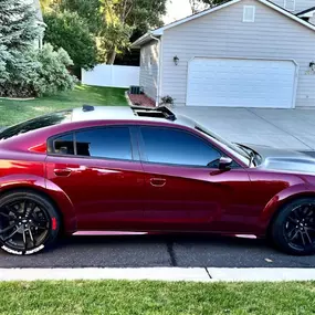 A sporty dark red Dodge Charger parked on a residential street. The vehicle features deeply tinted side and rear windows, showcasing a sleek, private look achieved through window tinting.