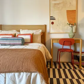 A bed with a brown blanket and a red chair in front of a painting