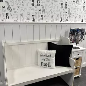 A white bench with playful dog-themed pillows and decor provides a cozy waiting area for guests in the Exeter lobby. Retail leashes are also displayed nearby for easy access.