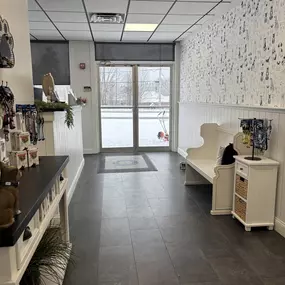 Clean and organized lobby view facing the glass entry at Playtime Pet Resort Exeter. The space features custom dog wallpaper, retail shelving, and guest seating, creating a welcoming atmosphere.