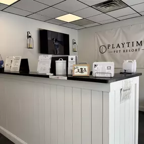 The front desk at Playtime Pet Resort Exeter is neatly organized with pet care materials, branded signage, and a mounted TV showing happy pets in action.