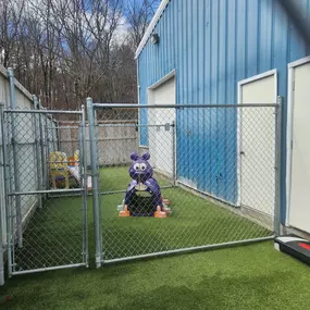 Outdoor fenced play yard at the Windham location with artificial turf and colorful playground equipment, designed for safe and fun outdoor enrichment.