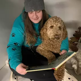 A team member shares a quiet moment reading to a dog inside a cozy suite at Playtime Pet Resort Windham, part of their enrichment and bonding programs.